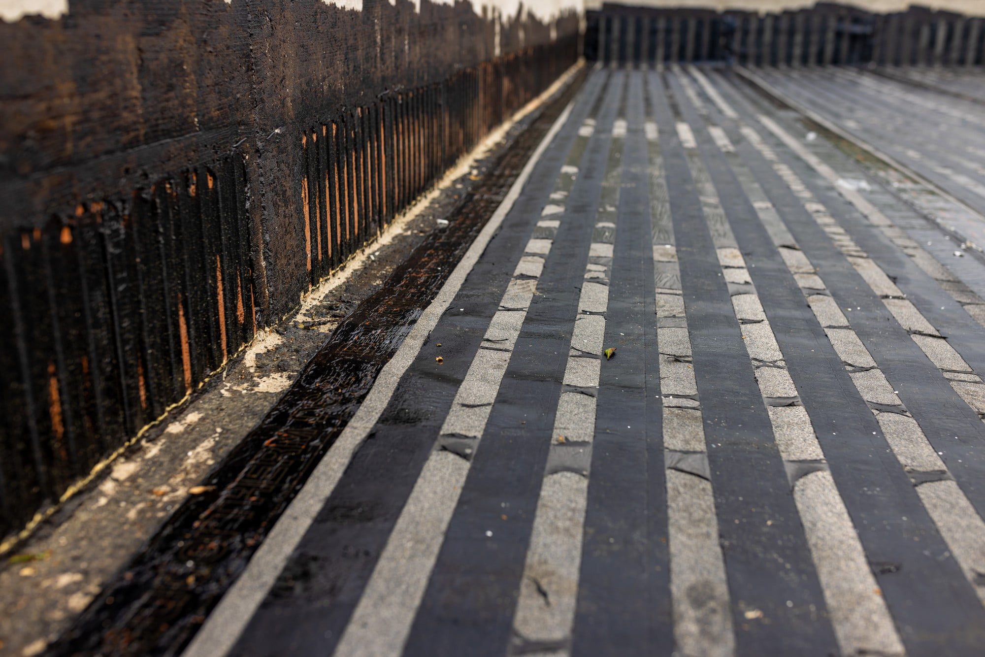 Sure, here is a detailed alt text description of the image provided:"A construction worker is using a torch flame to weld a vapour barrier on a new flat roof. The worker, wearing protective gloves and gear, focuses intently on the task. The vapour barrier material appears dark and smooth, while the flat roof surface beneath is clean and well-prepared. The background shows a clear sky indicating good weather. The process creates a secure and sealed layer intended to prevent moisture from penetrating the roof structure."Feel free to ask if you need any specific features in the description!